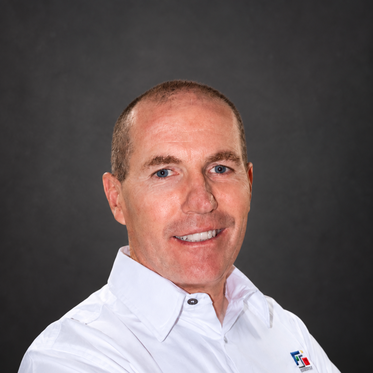 Portrait of a man in a white AFI Consult shirt against a dark background